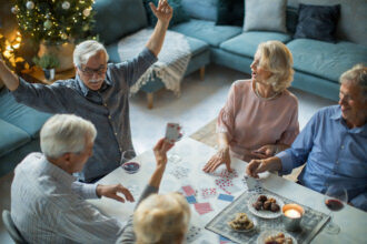 Persone che giocano a carte davanti intorno a un tavolo con biscotti e vino
