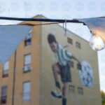 Dipinto di un bambino con pallone su un palazzo con in primo piano una lampadina